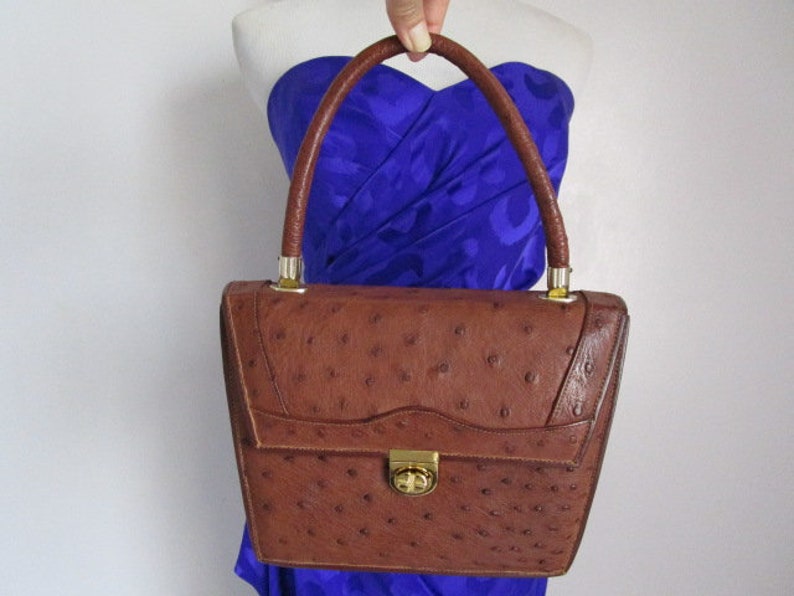May include: A brown ostrich leather handbag with a gold clasp and a top handle.