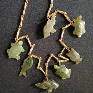 May include: A gold chain necklace with green jade pendants shaped like fish and turtles.