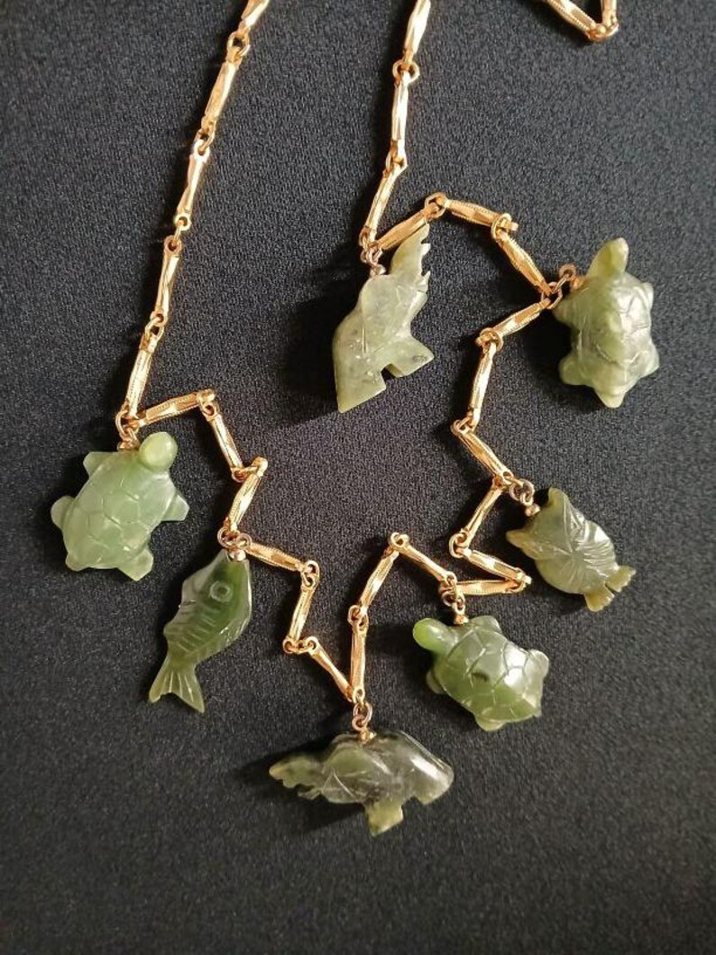 May include: A gold chain necklace with green jade pendants shaped like fish and turtles.