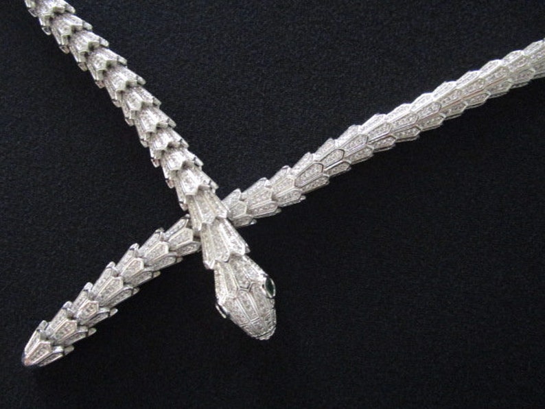 Op de afbeelding: Een zilveren slangenketting met een dubbel slangenontwerp. De ketting is gemaakt van metaal en heeft een glanzende afwerking. De slangen zijn met elkaar verweven en hebben een gedetailleerd ontwerp.