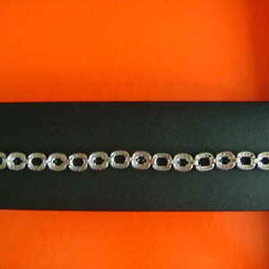 May include: A silver bracelet with a chain of square links, each set with small black stones.