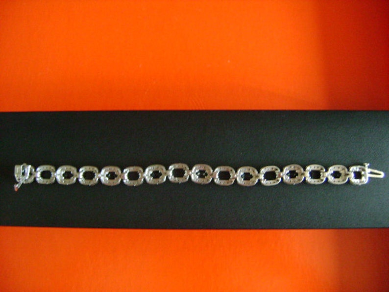 May include: A silver bracelet with a chain of square links, each set with small black stones.