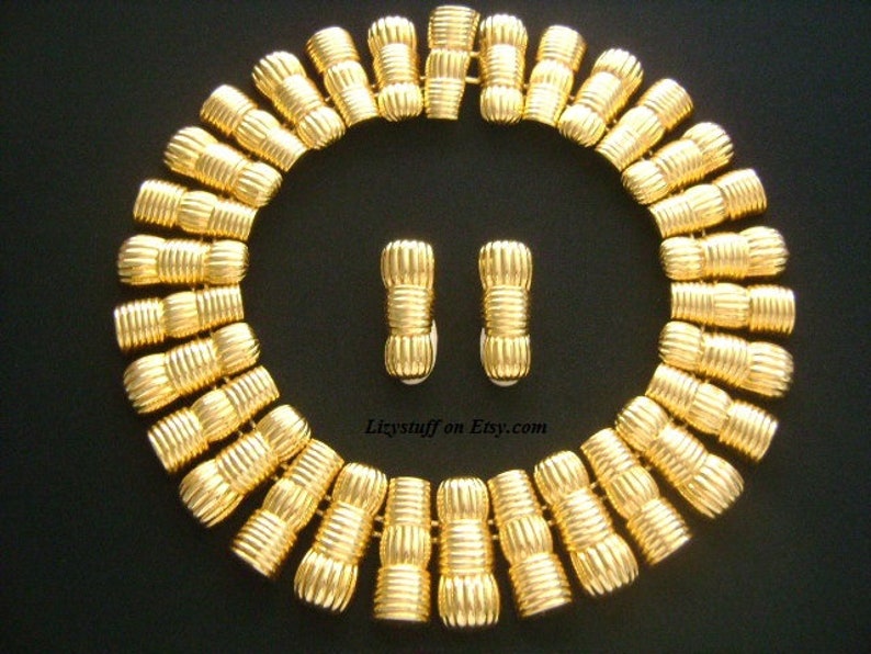 May include: A gold-tone necklace and matching earrings set. The necklace is made of a series of linked, textured, cylindrical beads. The earrings are a similar design.