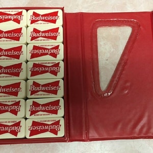 May include: A set of white dominoes with red Budweiser logos and the text "King of Beers". The dominoes are in a red case with a clear plastic window.