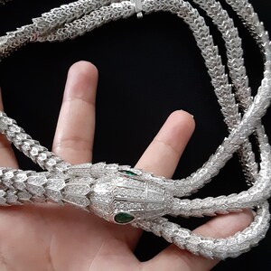 Peut inclure: Un collier en argent en forme de serpent avec un pendentif t&ecirc;te de serpent incrust&eacute; de pierres claires et d'yeux verts.