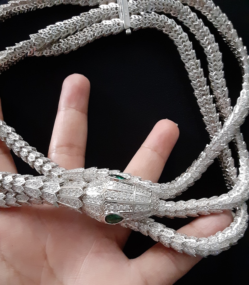 Peut inclure: Un collier en argent en forme de serpent avec un pendentif t&ecirc;te de serpent incrust&eacute; de pierres claires et d'yeux verts.