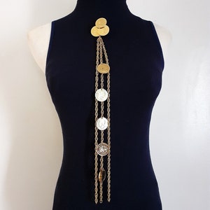 May include: A gold chain necklace with multiple gold and silver coin-shaped pendants. The necklace is displayed on a black mock neck shirt.