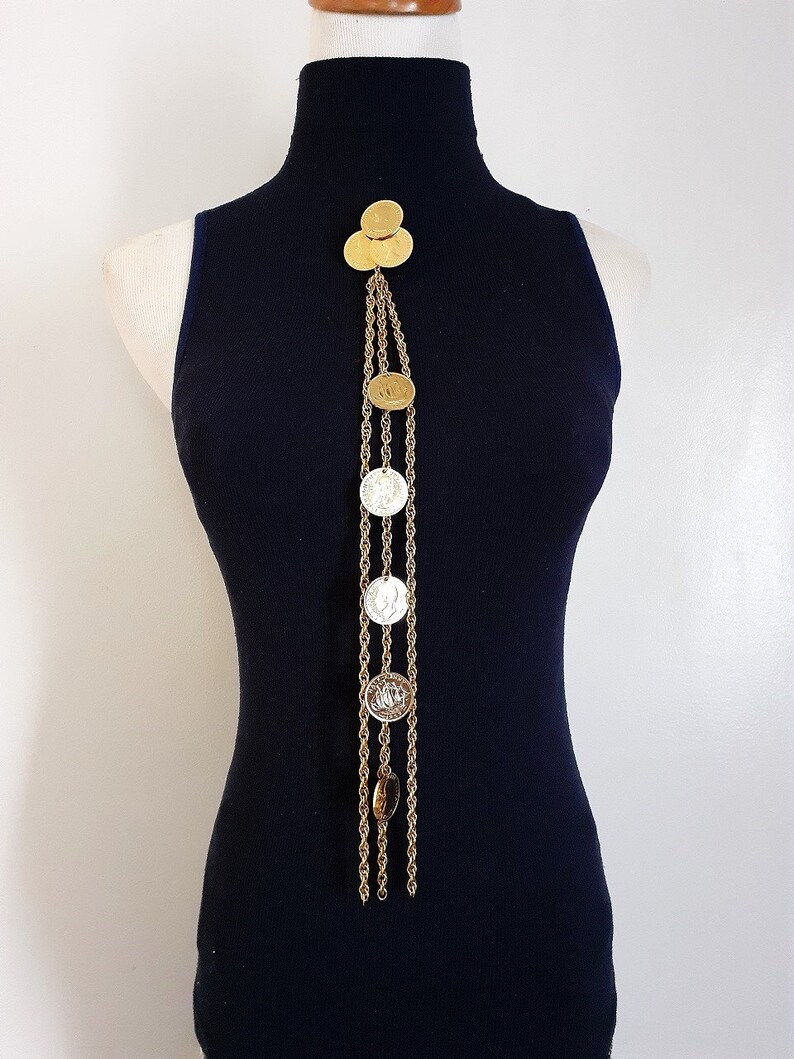 May include: A gold chain necklace with multiple gold and silver coin-shaped pendants. The necklace is displayed on a black mock neck shirt.