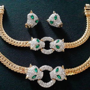Op de afbeelding: Een gouden ketting collier en armband set met groene en heldere kristallen panterkop accenten.