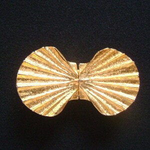 May include: A gold-tone metal belt buckle shaped like a seashell. The buckle is made of two halves that open and close.