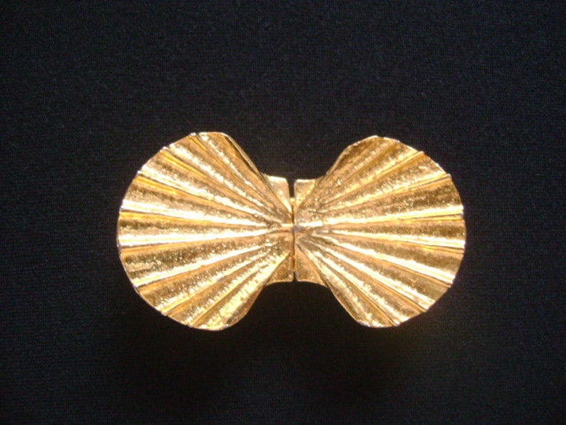 May include: A gold-tone metal belt buckle shaped like a seashell. The buckle is made of two halves that open and close.