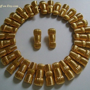 May include: A gold-tone necklace and matching earrings. The necklace is made of a series of linked, textured, cylindrical beads. The earrings are a pair of matching, textured, cylindrical beads.
