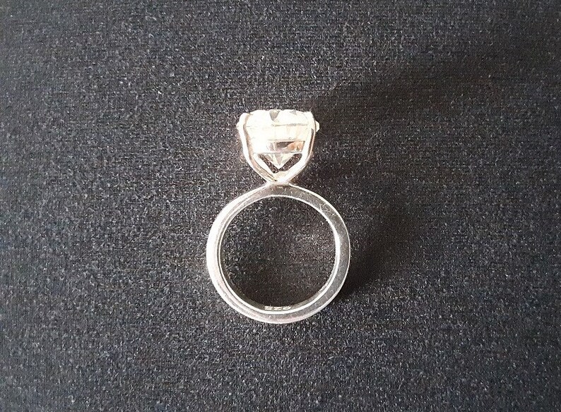 Op de afbeelding: Een zilveren ring met een grote, heldere, ronde edelsteen in een kraalbezetting.