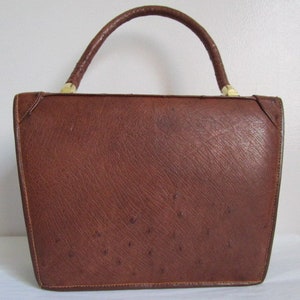 May include: A brown leather handbag with a top handle and a textured ostrich skin pattern.