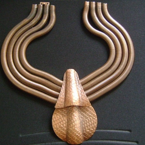 May include: A gold-toned necklace with a large, textured pendant. The necklace is made of multiple strands of linked metal.