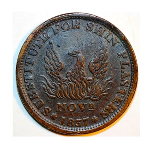 May include: A copper coin with the words "Substitute for Shin Plasters" and "Nov 1857" around the edge. A phoenix is in the center of the coin.