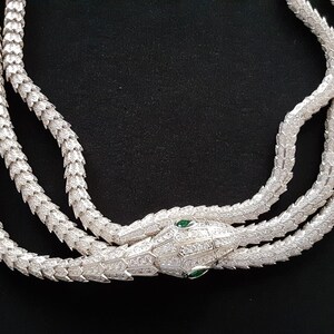 Peut inclure: Un collier de serpent en argent avec un pendentif t&ecirc;te de serpent. La t&ecirc;te de serpent est incrust&eacute;e de pierres claires et a deux yeux verts.