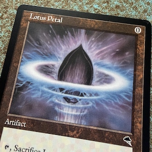 May include: A Magic: The Gathering trading card titled Lotus Petal, featuring a dark, pointed central object surrounded by a glowing blue ring of energy against a purple background, with a zero mana cost symbol in the top right corner.