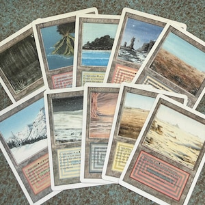 May include: A collection of nine Magic: The Gathering dual land trading cards arranged in a fan shape. Each card features unique landscape artwork, white borders, and text boxes detailing mana abilities and game rules for each specific land type.