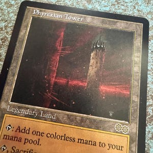 May include: A Phyrexian Tower trading card featuring a dark, atmospheric illustration of a tall, jagged tower against a deep red and black sky. The card text includes the title Phyrexian Tower and the classification Legendary Land in white font.