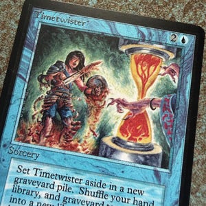 May include: A blue Magic: The Gathering trading card titled Timetwister. The illustration depicts a figure holding a sword near a glowing orange hourglass, with a clawed hand reaching toward it. The card text reads Sorcery and includes game rules.