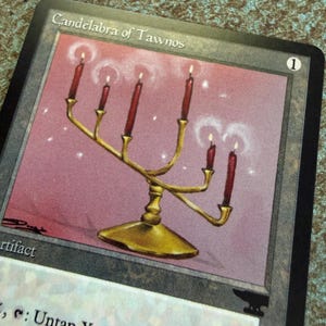 May include: A trading card titled Candelabra of Tawnos featuring an illustration of a gold candelabra with six lit red candles against a light purple background. The card has a black border, a number 1 in a circle, and the word Artifact printed.