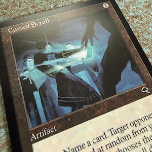 May include: A Magic: The Gathering trading card titled Cursed Scroll, featuring an illustration of figures in dark clothing reaching toward a glowing blue light. The card has a black border, a cost of 1, and the text Artifact printed at the bottom.