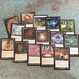 May include: A collection of Magic: The Gathering trading cards, featuring various artifact and creature cards. The cards have detailed illustrations and text, with a mix of colors and designs. Some cards include text like "Mox Diamond" and "Metalworker".