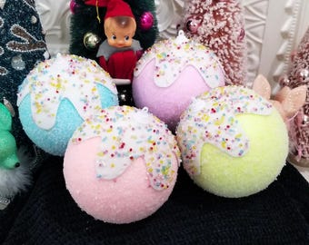 May include: Four colorful Christmas ornaments with a frosted, sprinkle-covered design. The ornaments are in shades of blue, pink, and yellow, with white frosting and colorful sprinkles. These decorative ornaments are perfect for adding a festive touch to any holiday decor.