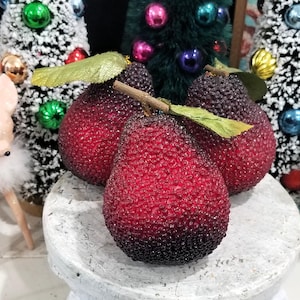 May include: Three decorative pears with a textured, beaded surface that transitions from a deep dark red at the base to a lighter red at the top. Each pear features a brown stem and a single green fabric leaf attached to the top of the fruit.