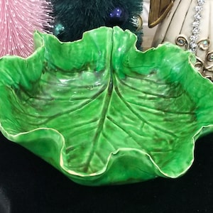 May include: A green ceramic bowl shaped like a cabbage leaf. The bowl has a glossy finish and is perfect for serving snacks or salads.