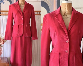May include: A pink velvet suit with a blazer and skirt. The blazer has a notched collar, three buttons, and two patch pockets. The skirt is knee-length and has a straight silhouette.