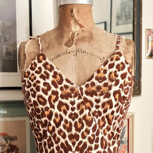 May include: A vintage-style dress with a brown and white leopard print pattern. The dress features a V-neckline and spaghetti straps. The dress is displayed on a vintage dress form.