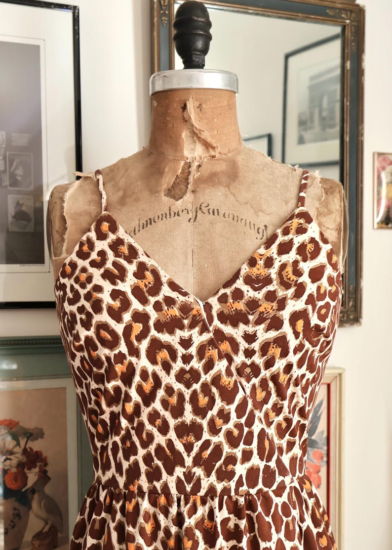 May include: A vintage-style dress with a brown and white leopard print pattern. The dress features a V-neckline and spaghetti straps. The dress is displayed on a vintage dress form.
