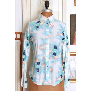 Peut inclure: Une chemise blanche à manches longues à boutons avec un imprimé abstrait coloré comprenant des formes géométriques, des nuages et un motif bleu et vert.