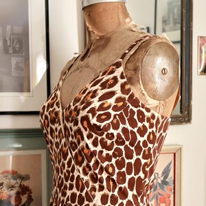 May include: A vintage-style dress with a brown and cream leopard print pattern. The dress features a V-neckline and spaghetti straps. The dress is displayed on a vintage dress form.