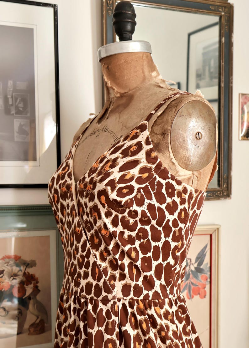 May include: A vintage-style dress with a brown and cream leopard print pattern. The dress features a V-neckline and spaghetti straps. The dress is displayed on a vintage dress form.