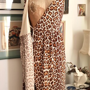 May include: A vintage leopard print dress on a mannequin. The dress features a brown and cream animal print pattern. The dress has spaghetti straps and a draped design. The mannequin is a vintage style with a cream-colored torso.