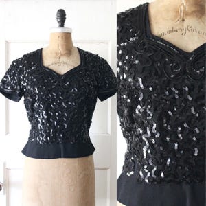Puede incluir: Top negro con lentejuelas, mangas cortas y escote en V. El top está adornado con lentejuelas y abalorios, y tiene la cintura entallada. La prenda se exhibe en un maniquí sobre un fondo blanco.