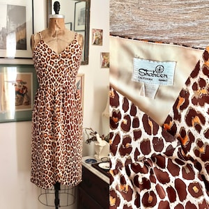 May include: A vintage leopard print dress with spaghetti straps and a V-neck. The dress is displayed on a mannequin. The fabric features brown and orange spots on a cream background. The label reads "Shaheen California Hawaii."