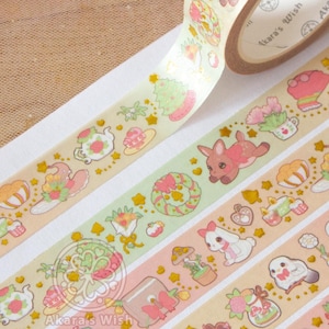 May include: Four rolls of washi tape with a pastel pink, yellow, and green background. Each roll features a different design with gold accents and illustrations of animals, plants, and teacups. The text "Akara's Wish" is printed on the tape.