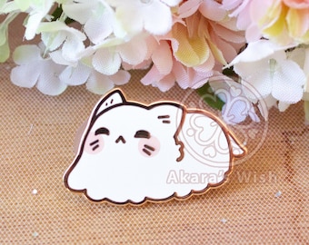 May include: A white cat enamel pin with a cute design. The pin features a cat with a light brown outline and blush. The cat is lying down with a patterned design on its back. The pin is on a brown surface with flowers in the background.