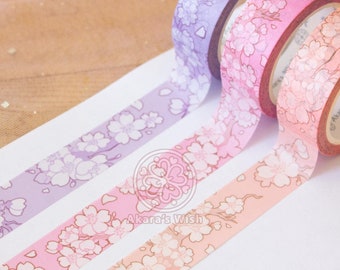 Puede incluir: Tres rollos de cinta washi con un diseño floral. La cinta es en tonos de rosa, morado y melocotón. La cinta está etiquetada "Akara's Wish".