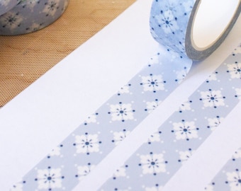 May include: Three rolls of blue and white patterned washi tape with a snowflake design. The tape is unrolled on a white surface, showing the pattern.