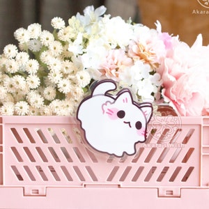 May include: A pink plastic storage crate with a white cartoon cat sticker on the front. The crate is filled with white and pink flowers.