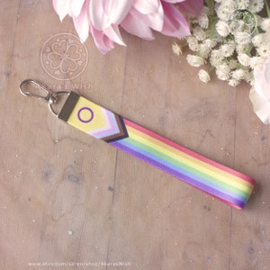 May include: A yellow, purple and brown lanyard with a rainbow stripe and a purple circle with a yellow ring. The lanyard has a silver metal clasp.