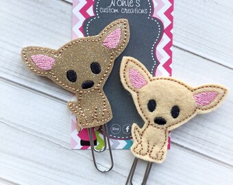 May include: Two felt chihuahua dog paper clips. One is brown with glitter and the other is beige. Both have pink ears and black eyes. The paper clips are attached to a card that says "Nonie's custom creations".