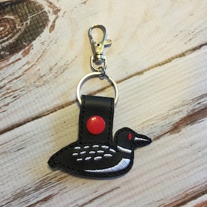 May include: Black leather keychain with a red button and an embroidered loon design.
