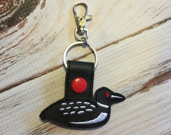 May include: Black leather keychain with a red button and an embroidered loon design.