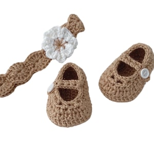 May include: A set of crocheted baby shoes and a headband. The shoes are brown and have a white button on each. The headband is brown with a white crocheted flower.